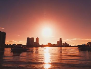 Silhouette buildings by river against sky during sunset