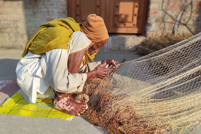 A very old but capable exemplary man of india making fishing nets in the sun 