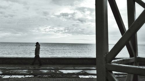 Man walking on promenade by sea against sky