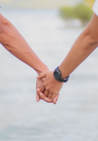 Close-up of couple hands against sea