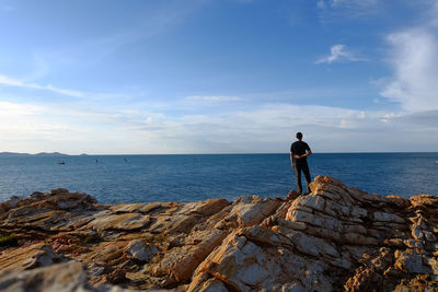 Man standing on rock by sea against sky