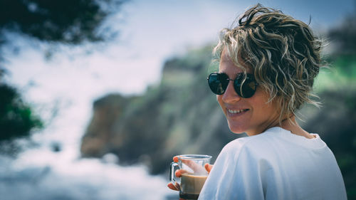 Portrait of smiling woman in sunglasses drinking tea outdoors