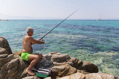 Fisherman sitting on a rock and fishing with a rod