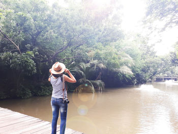 Woman standing by lake against trees