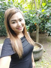 Portrait of smiling young woman standing against plants