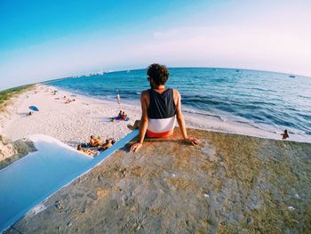 Rear view of man relaxing at beach against sky