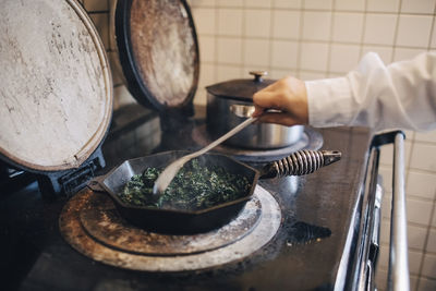 Cropped hand of chef stirring kale in cooking pan on stove at restaurant kitchen