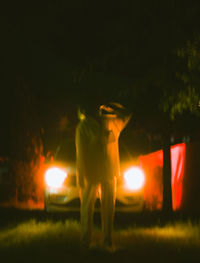 Rear view of man standing on illuminated street at night