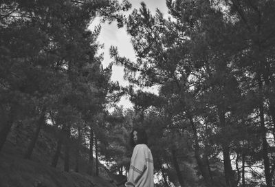 Rear view of woman standing amidst trees and looking back, in forest