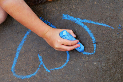 Cropped hand of girl drawing on road