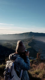 Side view of woman photographing on mountain against sky