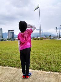 Rear view full length of girl saluting flag on field