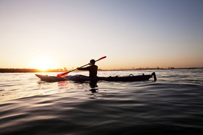 Rear view of man kayaking in sea against clear sky