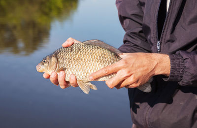 Midsection of man holding fish by lake