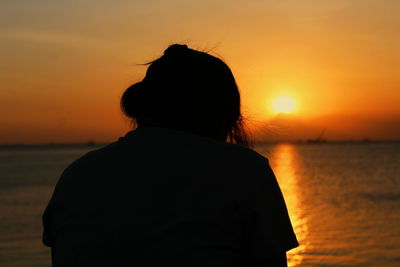 Rear view of silhouette woman standing at beach during sunset