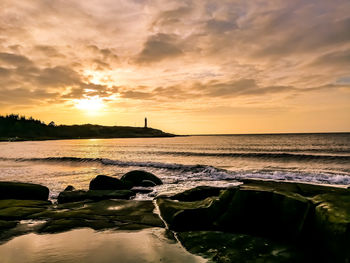 Scenic view of sea against sky during sunset with a lighthouse in the background 