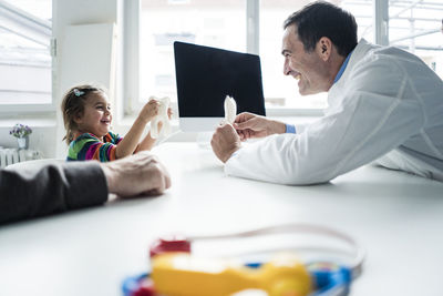 Doctor and happy girl with tooth model at desk in medical practice