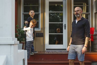 A father stands on his front stoop with his two small boys