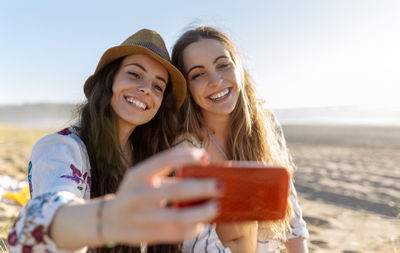 Two best friends taking selfie with smartphone on the beach