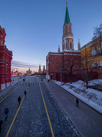 People walking on street amidst buildings against blue sky during winter