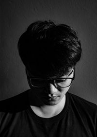 Close-up of young man wearing eyeglasses standing against wall