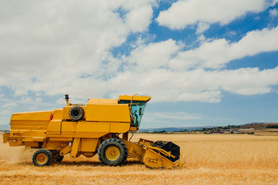 Yellow tractor plowing field and collecting ears