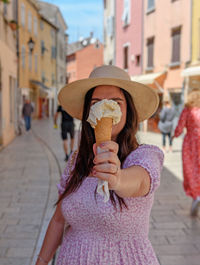 Portrait of young woman standing in street of colorful old town, holding ice cream in cone