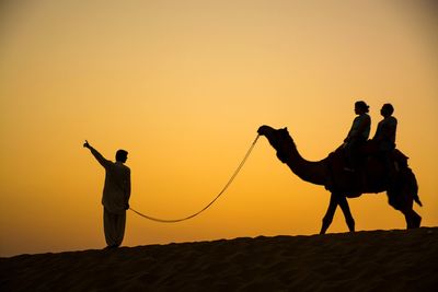 Silhouette people on desert against clear sky during sunset