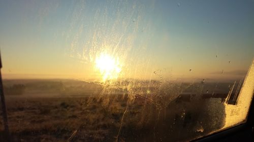 Close-up of wet window against sky during sunset