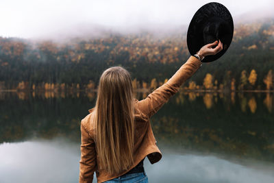 Rear view of woman standing by lake against sky