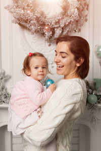 Cheerful mother carrying daughter during christmas at home