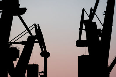 Low angle view of silhouette cranes against clear sky