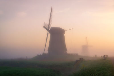 Traditional windmill on field against sky during sunset