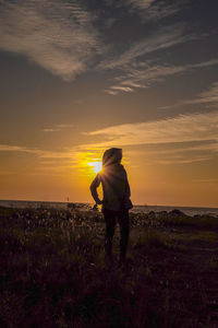 Rear view of woman standing on field against sky during sunset