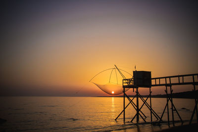 Silhouette cranes by sea against sky during sunset