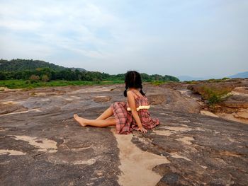 Girl sitting on rock against sky