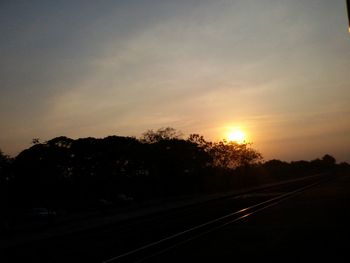 Road amidst silhouette trees against sky during sunset