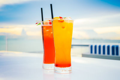 Close-up of drinks on table against sea during sunset