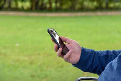 Cropped hand of man using mobile phone on field