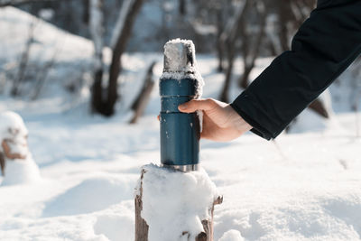 Male hand holding a thermos outside. sunny day, winter snowy forest. hiking, camping concept