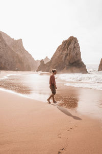 Rear view of woman standing at beach against clear sky