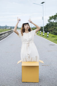 Young woman holding placard while standing in cardboard box on road