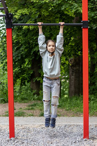 Young girl hanging on red horizontal bar in outdoor playground