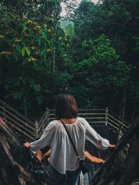 Rear view of man standing by railing in forest