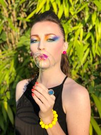 Close-up portrait of young woman blowing bubble against plants