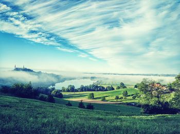 Scenic view of landscape and lake against cloudy sky during foggy weather