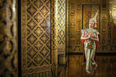 Portrait of woman with hands clasped standing against wall in temple