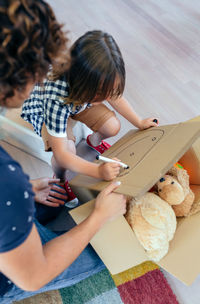 Father kneeling by son writing on cardboard box at home