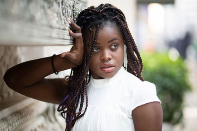 Beautiful young woman looking away while standing by wall