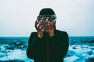 Man holding umbrella against sea against clear sky